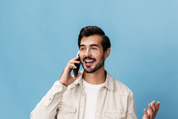 Close-up portrait of a brunette man talking on the phone with a friend smiling with teeth, on a blue background in a white T-shirt and jeans, copy space