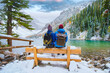 Lake Agnes by Lake Louise Banff National Park with snowy mountains in the Canadian Rocky Mountains during winter. A couple of men and women sitting on a bench by the emerald green lake in Canada with