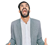 Young Hispanic Man Wearing Business Clothes Angry And Mad Screaming Frustrated And Furious, Shouting With Anger. Rage And Aggressive Concept.