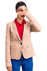 Sticker - Young beautiful woman wearing business shirt and glasses peeking in shock covering face and eyes with hand, looking through fingers with embarrassed expression.