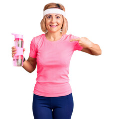 Sticker - Young blonde woman wearing sportswear holding water bottle pointing finger to one self smiling happy and proud