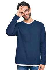 Wall Mural - Young hispanic man wearing casual clothes and glasses doing ok gesture with hand smiling, eye looking through fingers with happy face.