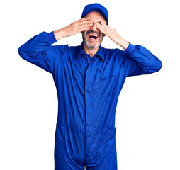 Canvas Print - Middle age handsome man wearing mechanic uniform covering eyes with hands smiling cheerful and funny. blind concept.