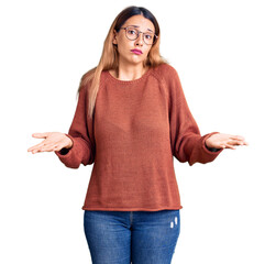 Canvas Print - Beautiful young woman wearing casual clothes and glasses clueless and confused expression with arms and hands raised. doubt concept.