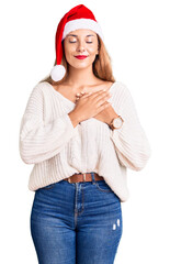 Sticker - Beautiful young woman wearing christmas hat smiling with hands on chest with closed eyes and grateful gesture on face. health concept.