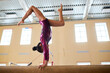 © Seventyfour - Side view of female in purple costume doing double stag handstand on gymnastic balance beam, copy space