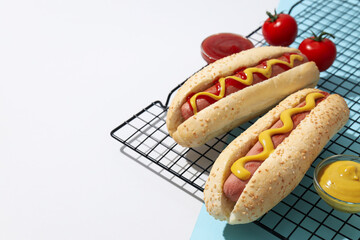 Wall Mural - Hot dogs on grid, sauces in bowls and tomatoes on white and blue background, space for text