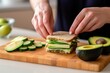 person assembling an avocado and cheese sandwich