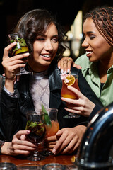  alluring and stylish multiracial girlfriends smiling and holding delicious cocktails in bar