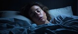 Fototapeta  - Middle aged woman lying awake in her bed at night because of insomnia stress fears nightmares or illnesses like fibromyalgia. Website header. Creative Banner. Copyspace image