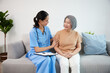caregiver or nursing home touching arms and talking with senior woman on sofa