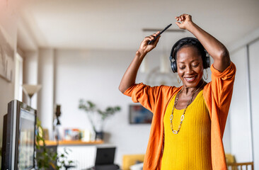 Woman listening to music with headphones connected to her smartphone in the living room at home
