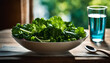 A white bowl filled with a fresh salad of lettuce, kale, and spinach sits on a wooden table, accompanied by a blue spoon and glass of water, appearing to be a wholesome and inviting meal.
