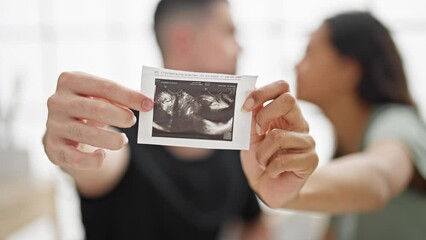 Wall Mural - Beautiful couple holding ultrasound baby sitting on bed kissing at bedroom