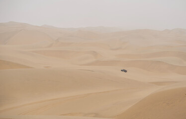 Sand dunes in the Namib desert, car in the distance 