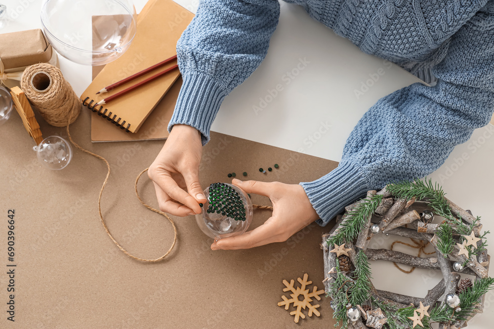 Woman decorating Christmas ball with rhinestones on table