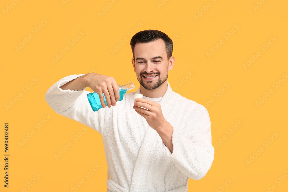 Handsome man with mouth rinse on yellow background