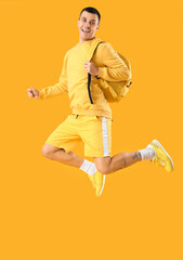 Poster - Male student with backpack jumping on yellow background