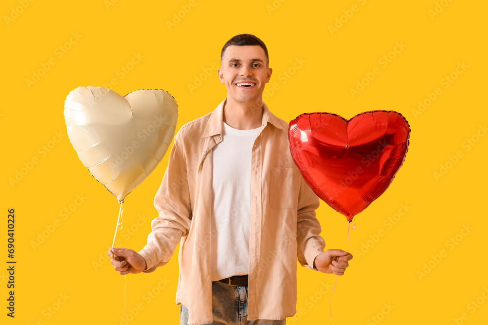 Young man with heart shaped air balloons on yellow background