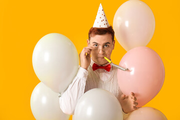 Sticker - Young man with party whistle and air balloons celebrating Birthday on yellow background