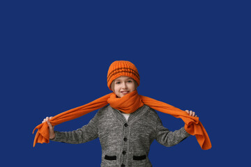 Wall Mural - Cute little happy boy in winter clothes on blue background