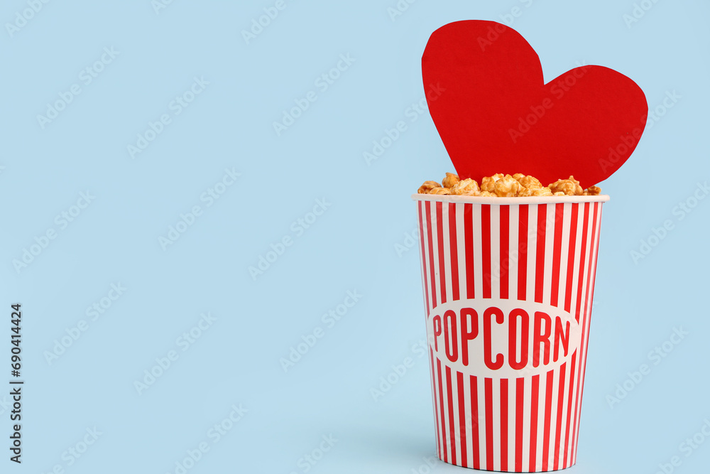 Bucket of popcorn with paper heart on blue background. Valentine's Day celebration