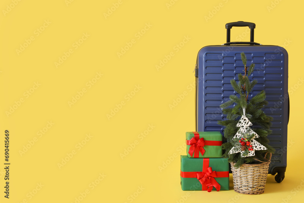 Suitcase with Christmas tree and presents on yellow background