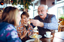 Happy Grandfather Eating Dessert With Grandchildren In Cafe