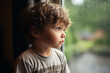Sad unhappy child looking at raindrops on the window.