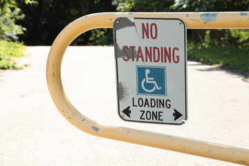 no standing loading zone with handicap symbol and two arrows pointing opposite direction mounted to yellow gate rail, white red blue and black