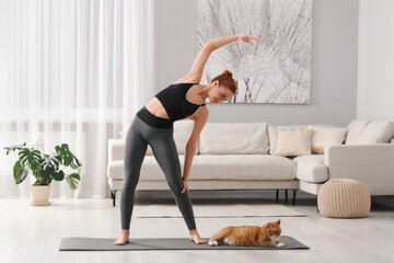 Poster - Beautiful woman with cute red cat practicing yoga on mat at home