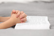 Girl holding hands clasped while praying over Bible indoors, closeup