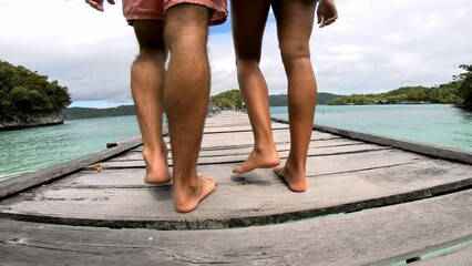 Wall Mural - People, legs and walking on pier, vacation and lake for adventure, fun and relaxing in back view. Couple, man and woman on romantic getaway for bond, caring and relationship with trip to Thailand