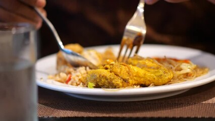 Wall Mural - An Indonesian woman eating fried rice or Nasi Goreng (indonesian) with spoon and fork at a restaurant. Selective focus.