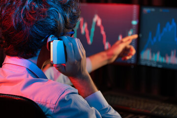 Young investor stock trader discussing on smartphone to broker, pointing with dynamic financial exchange investment on two laptop screens in current market graph in real time at modern office. Gusher.