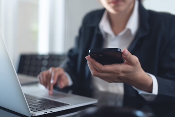 Canvas Print - Business woman using mobile phone during working on laptop computer, surfing the internet, searching business data at modern office. Asian businesswoman online working on computer at workplace