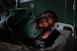 © ABCreative - African woman in hospital room, lying on her side, reading a book on her phone.