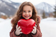 © Georgii - Beautiful young girl in winter outfit holding red heart-shaped balloon against the background of scenic winter mountain landscape. Cheerful Caucasian girl smiling happily. Valentine's Day concept.