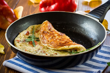 Wall Mural - Fried omelets with various autumn vegetables in a frying pan on a wooden table.