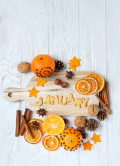 Sticker - decorated oranges, cinnamon sticks, cones, nuts and January text made of cookies on white wooden table. January month calendar concept. festive composition for winter season. flat lay