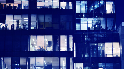 Wall Mural - Fragment of the glass facade of a modern corporate building at night. Big glowing windows in modern office buildings at night, in rows of windows light shines. Blue graphic filter.