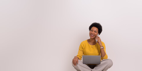 Happy female entrepreneur discussing over smart phone while working over laptop on white background