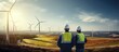 Two professional maintenance engineers in safety workwear using laptop and tablet checklist wind turbine on windmill construction farms Sustainable renewable energy and clean environment concep