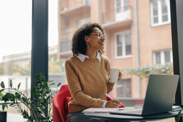 Wall Mural - Smiling woman entrepreneur working on laptop, making notes in cozy coworking space interior