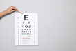 Ophthalmologist pointing at vision test chart on gray background, closeup. Space for text