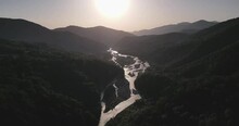 Aerial Footage Of A River Flowing Between Green Mountains With Dusk Sky In The Background At Sunset