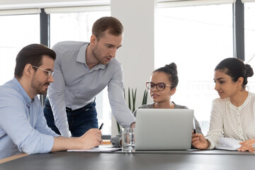 Wall Mural - Multiracial businesspeople sit at desk in boardroom look at laptop screen brainstorming over project together. Multiethnic diverse employees cooperate using computer, involved in team discussion.