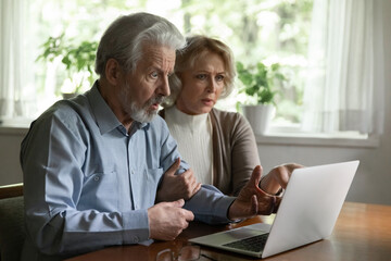 Unexpected problem with laptop. Shocked elderly spouses on pension look on pc screen getting personal information hacked. Aged family couple internet users feel scared reading scam blackmail message