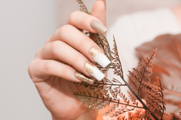 Wall Mural - Female hands with long nails with glitter nail polish. Long gold nail design. Women hand with sparkle manicure.