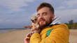 © Евгений Шемякин - Happy young man walking with his little pet Chihuahua or Toy terrier dog on the beach, hold puppy on hands. People love animals concept.